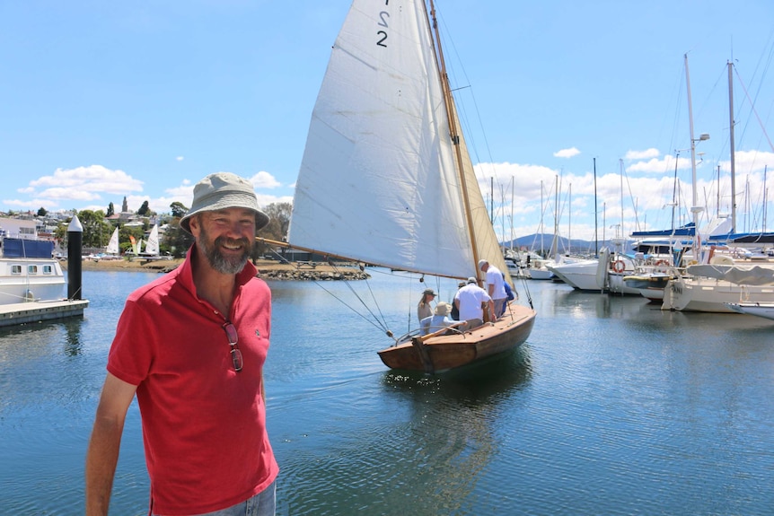 Maritime historian Colin Grazules poses in front of the restored Tassie Too as it sits in the water at a marina