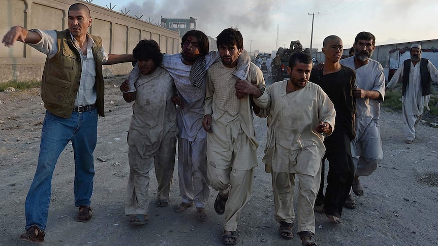 Afghan men carry a wounded man after a suicide attack