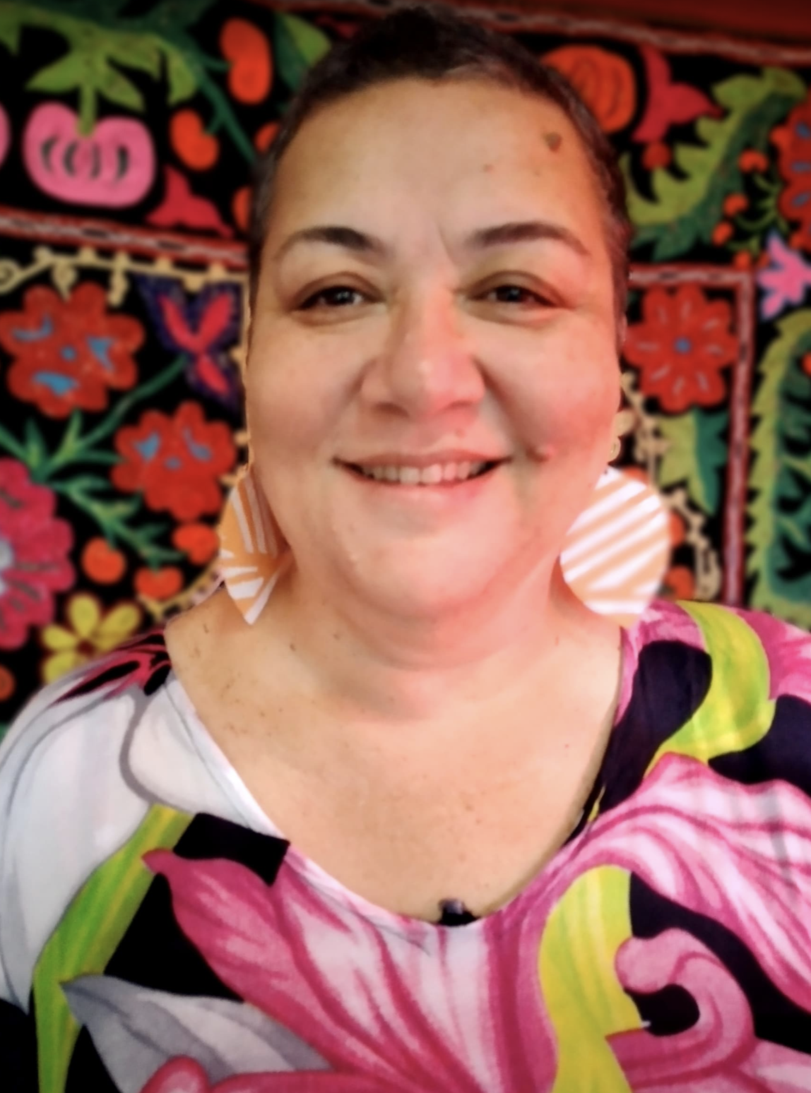 A woman with short hair standing in front of a wall with purple and pink flower designs 