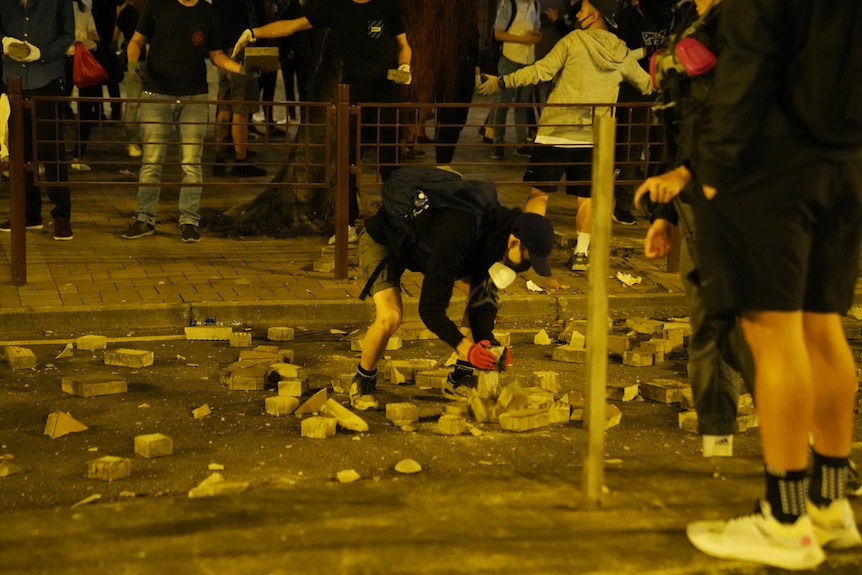 A black-clad protester breaks down bricks on a Hong Kong street as people behind him pass bricks around.