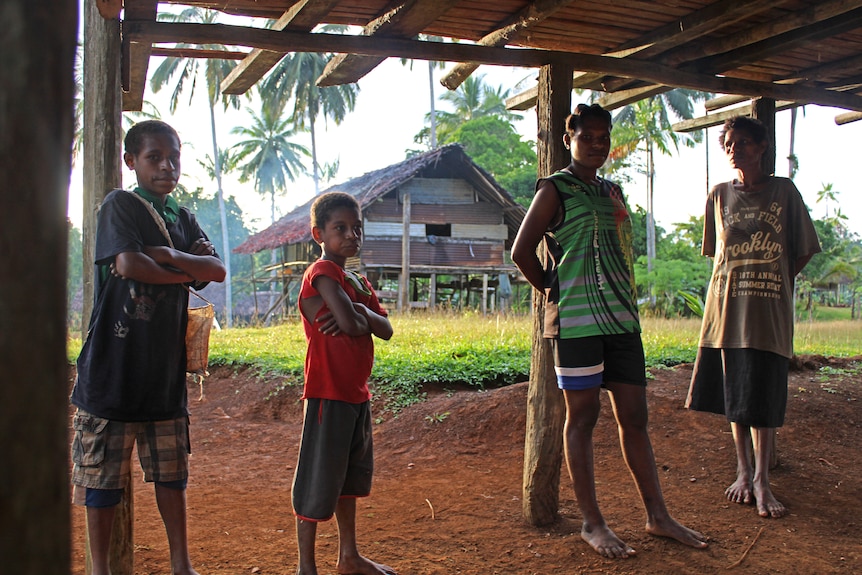 Four people stand underneath a building, two boys with arms folded.