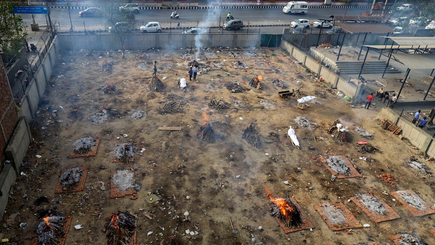 Rows of funeral pyres of covid victims burn in a patch of land next to a road that's being used for mass cremations