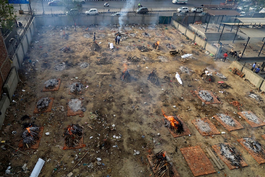 File di roghi funerari per le vittime del COVID-19 bruciano in un appezzamento di terreno vicino a una strada usata per cremare cadaveri di massa