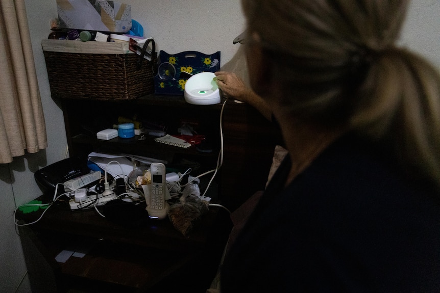 A woman reaches over to a white circular device sitting on a bedside table.