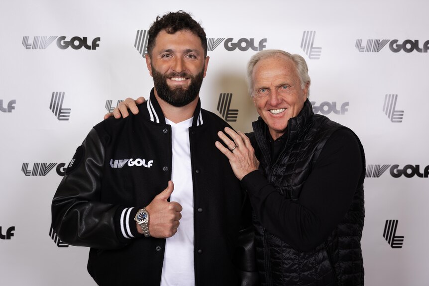 Jon Rahm smiles and gives a thumbs up while posing with Greg Norman