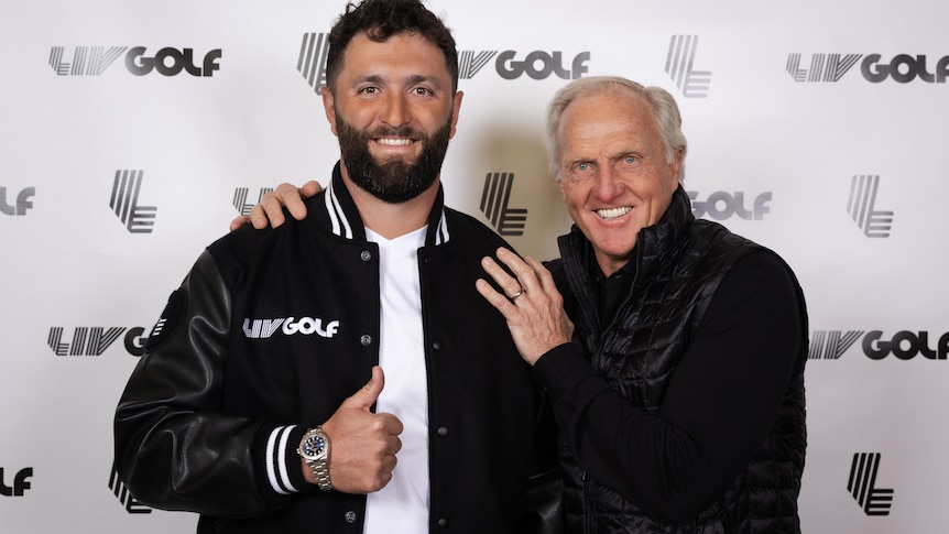 Jon Rahm smiles and gives a thumbs up while posing with Greg Norman