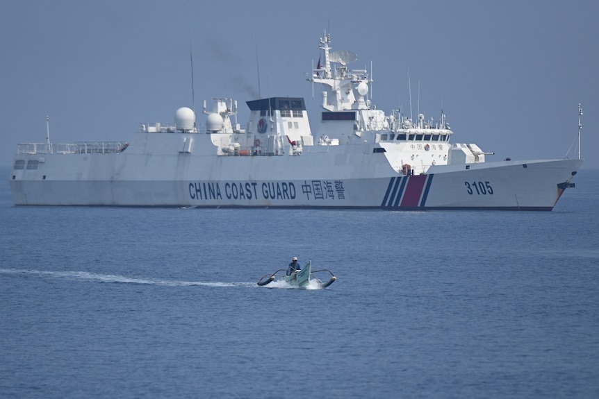 A Philippine fisherman aboard his wooden boat sailing past a Chinese coast guard ship. 