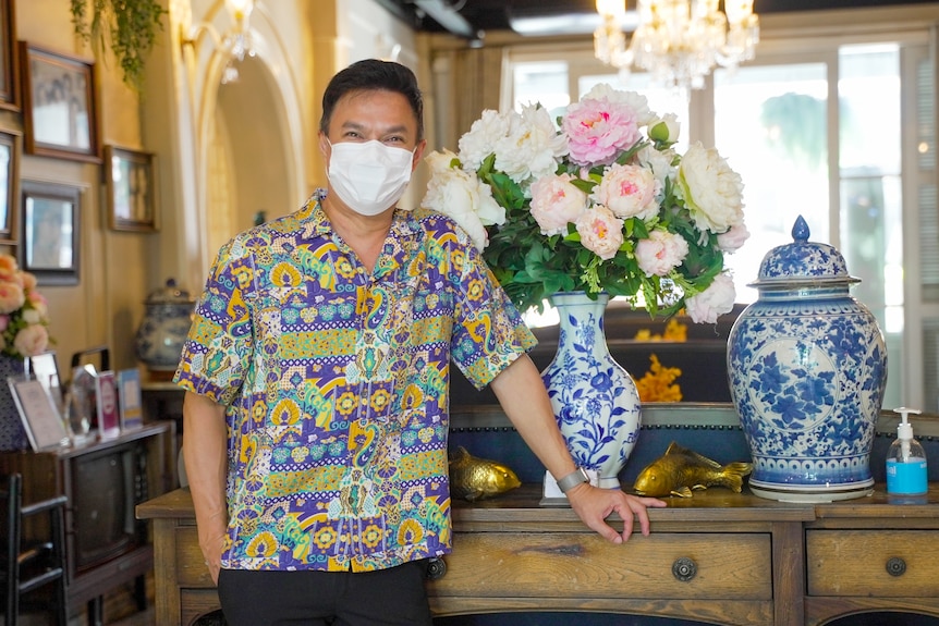 A Thai man in a bright shirt and face mask stands in hotel lobby