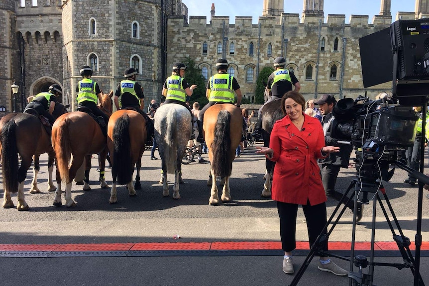 Lisa smiling with hands out standing in front of line of police on horses with rear ends facing camera.
