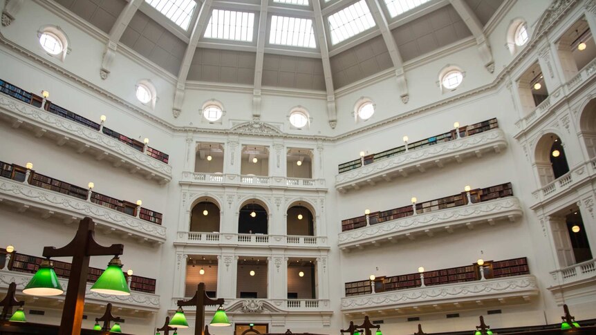 A large room with a high domed roof, balconies, bookshelves, long reading desks.