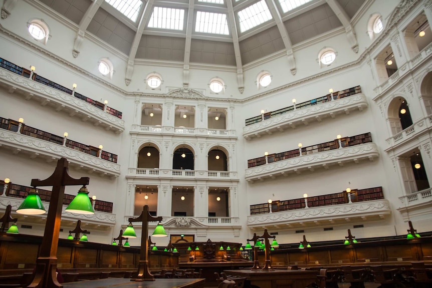 A large room with a high domed roof, balconies, bookshelves, long reading desks.