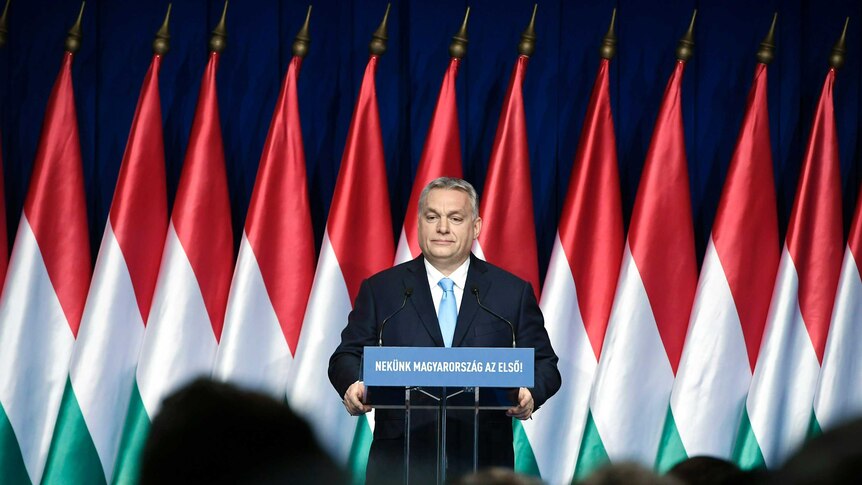 A man in a suit stands on stage at a podium