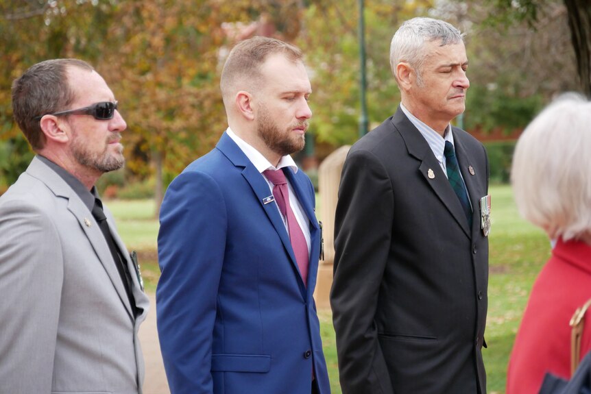 Three men stand with their heads looking down