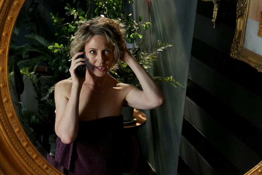 The actor, wearing a towel, stares into a mirror fixing her hair while she's on the phone.