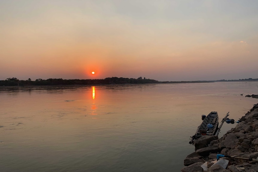 Two people look over the Mekong River as a net collects plastic rubbish