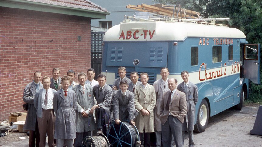 A group of men stand in front of a blue van marked "ABC TV".