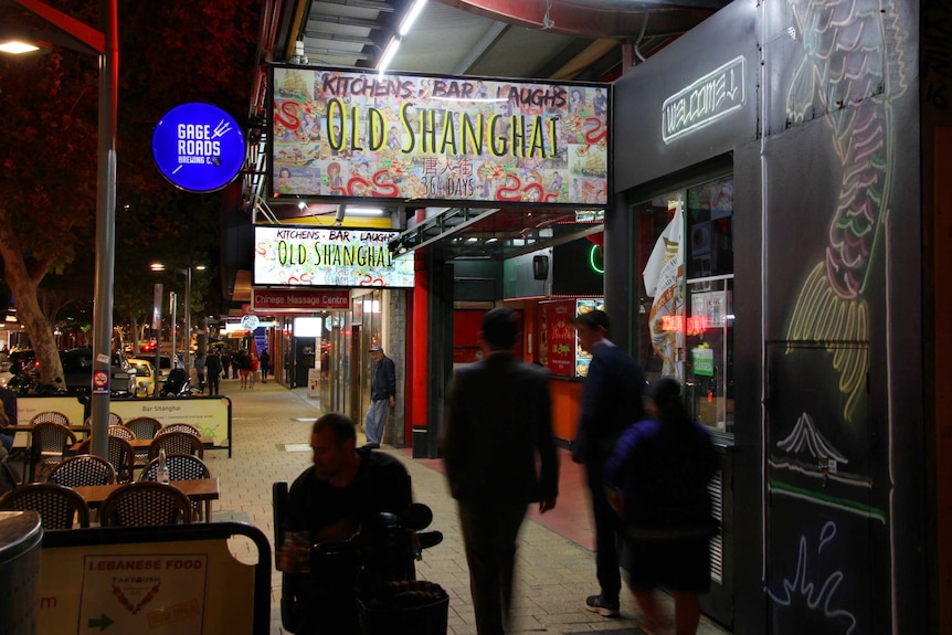 People walk and sit in front of a shopfront on an inner-city street