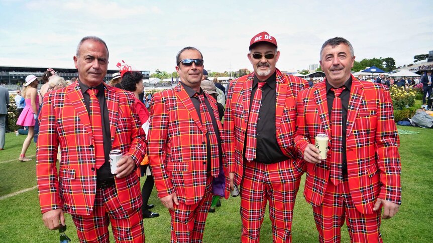 A group of four men in tartan suits and ties smile at the camera at the Melbourne Cup.