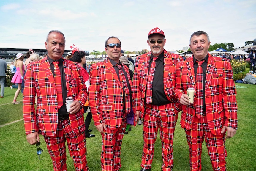 A group of four men in tartan suits and ties smile at the camera at the Melbourne Cup.