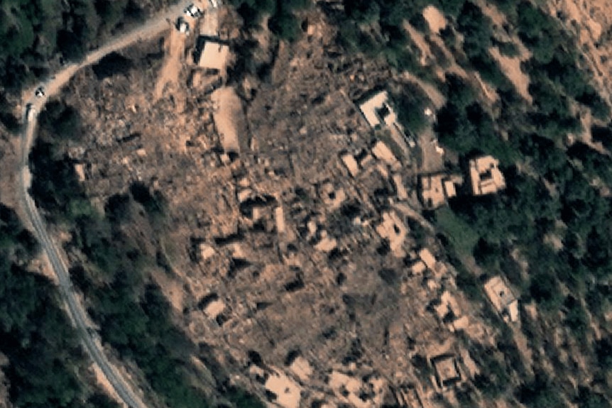 A birds eye view shows a small village surrounded by forest, with buildings almost completely flattened