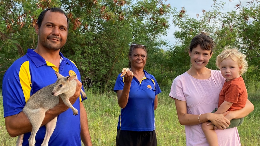 Four people stand in bushland smiling at camera