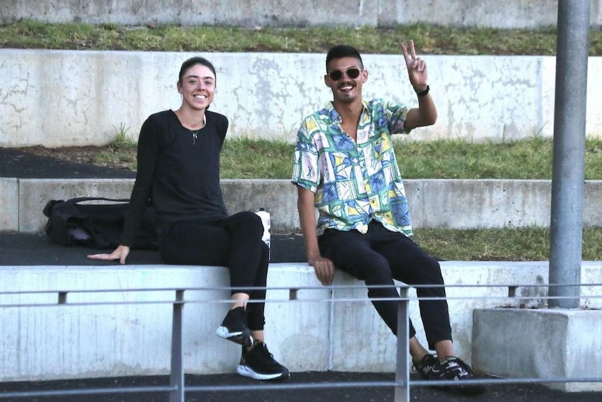 Matthew Clarke sits next to his girlfriend making a peace sign towards the camera.