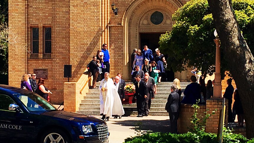 A coffin is carried from the church by a group of men.