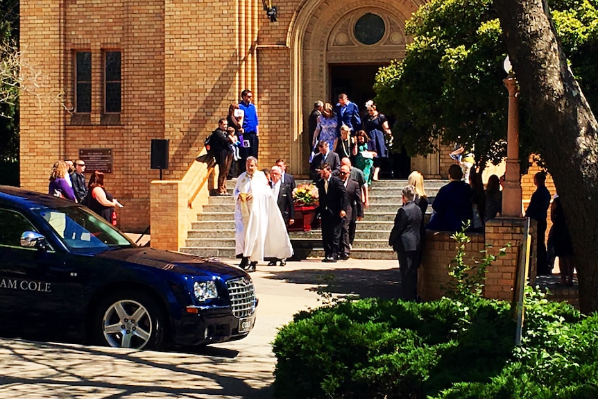 A coffin is carried from the church by a group of men.