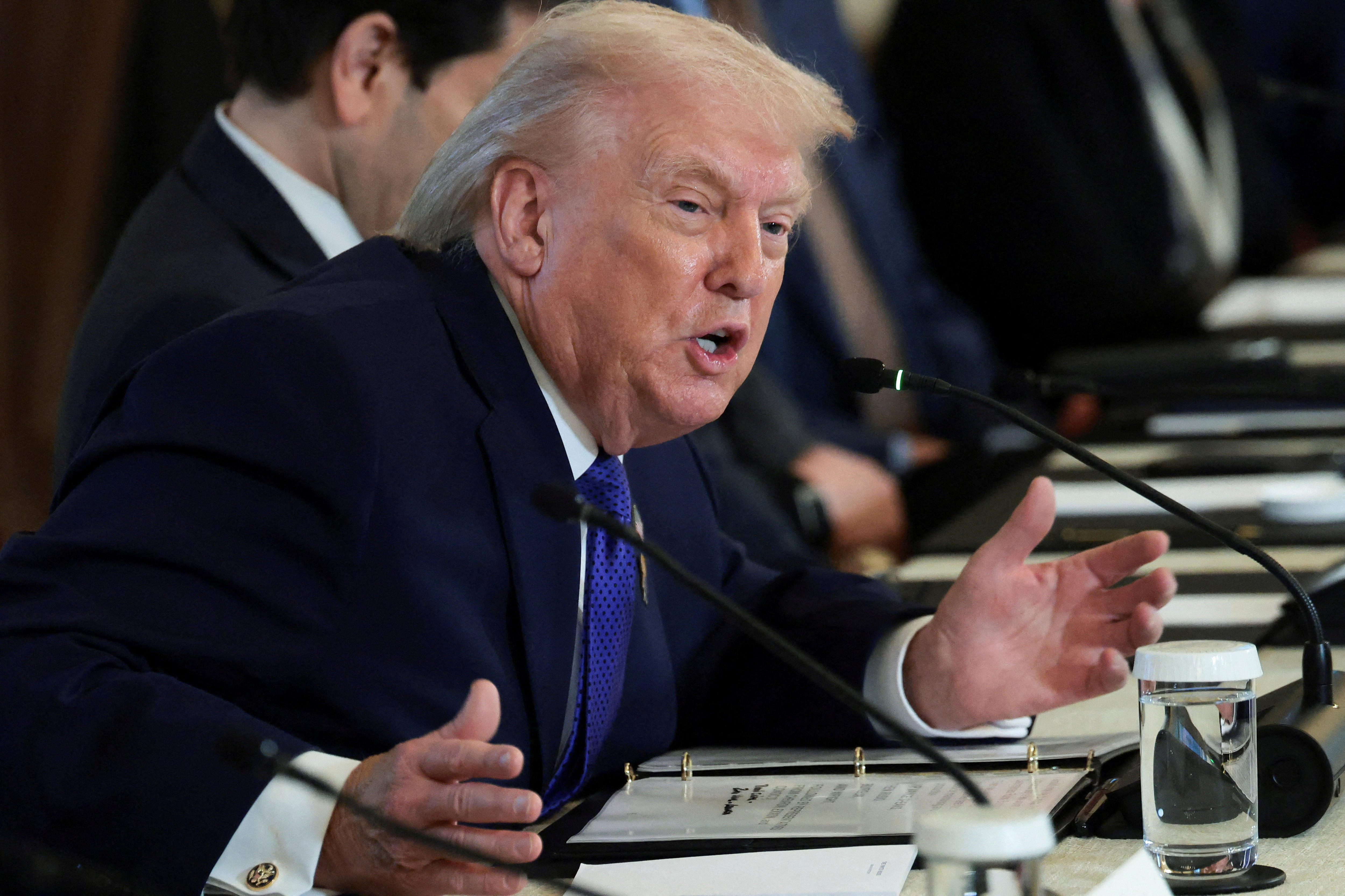 Trump se inclina sobre una mesa larga con las manos hacia afuera. 