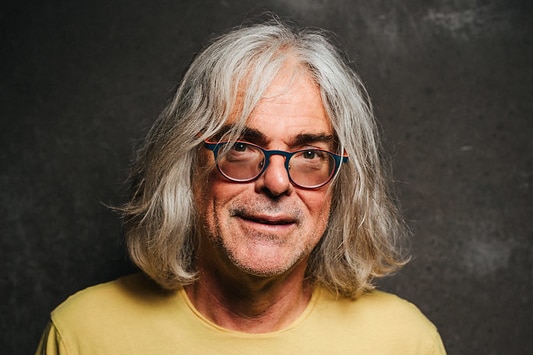 MONA founder David Walsh smiles as he poses for a portrait. He's wearing a bright shirt with a geometric pattern