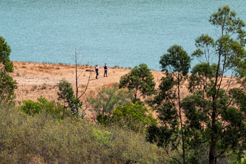 Two people seen in distance walking in front of large body of water.