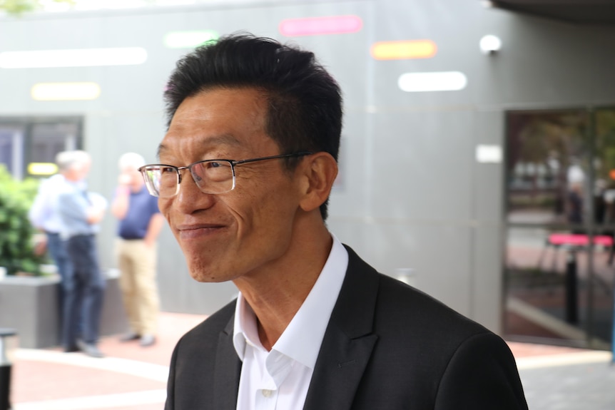 A man in a suit with glasses smiles.