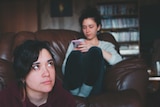 Woman sitting on the floor in front of woman on the couch on her phone