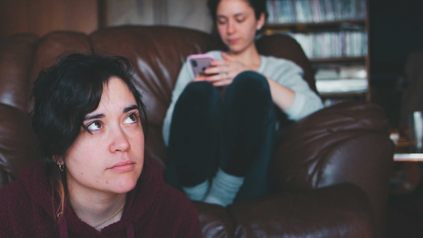 Woman sitting on the floor in front of woman on the couch on her phone