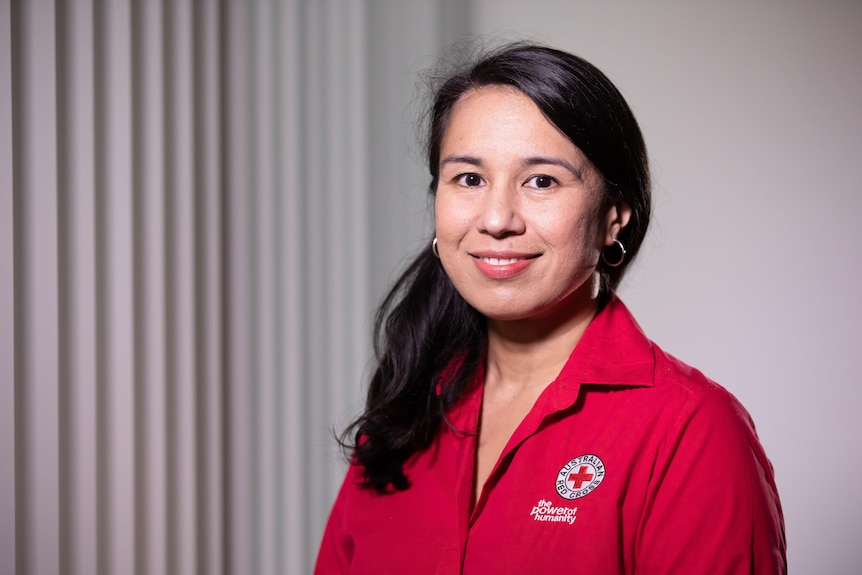 A woman in a branded Red Cross shirt, smiles.