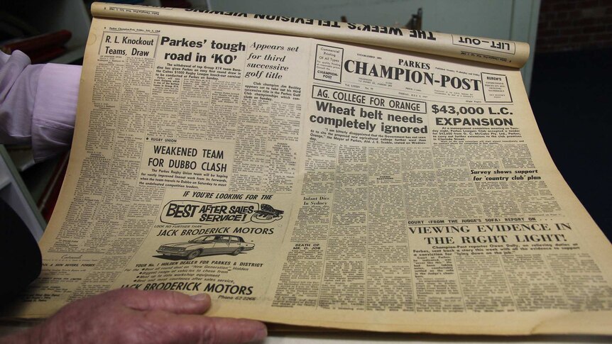 A faded yellow 1960s regional newspaper page held by a man's hands
