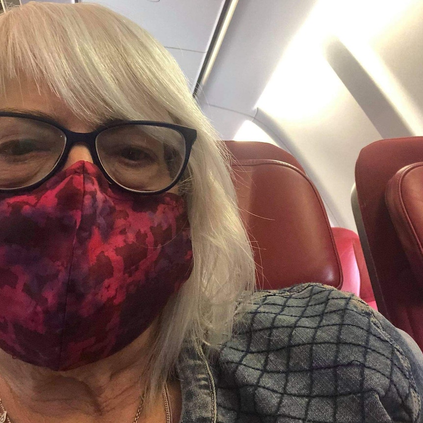 A selfie of a woman with glasses and wearing a mask sitting on an airplane