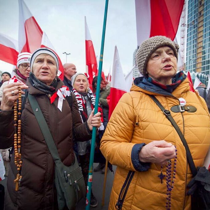 Women holding rosary beads protesting with flags behind them