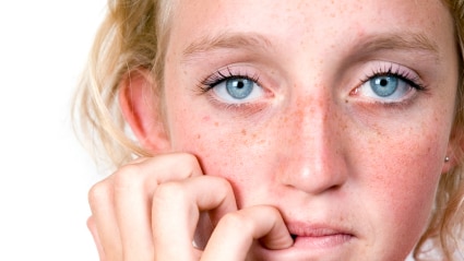 Woman with her hand near her mouth with an anxious expression on her face.