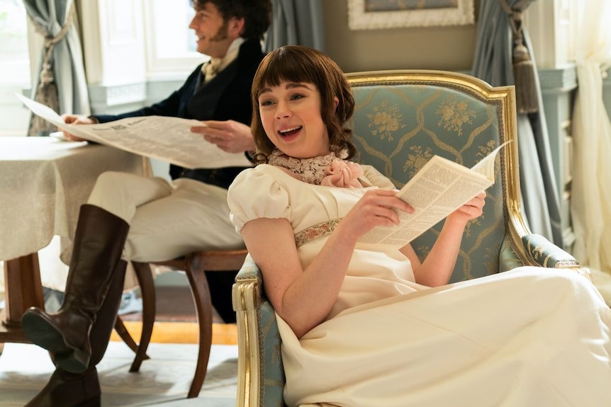 The character Eloise Bridgerton sits on a chair laughing.