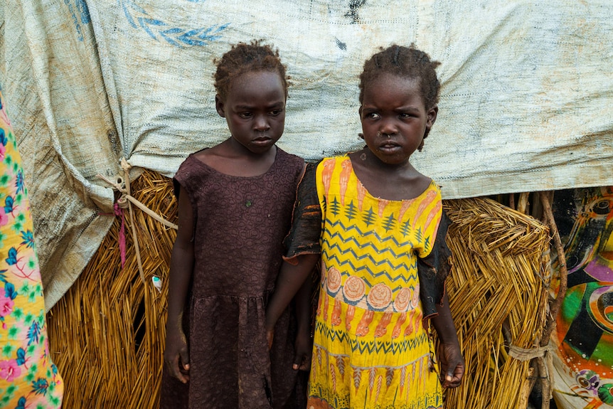 A close up of two children wearing dresses as they lean against a tent.
