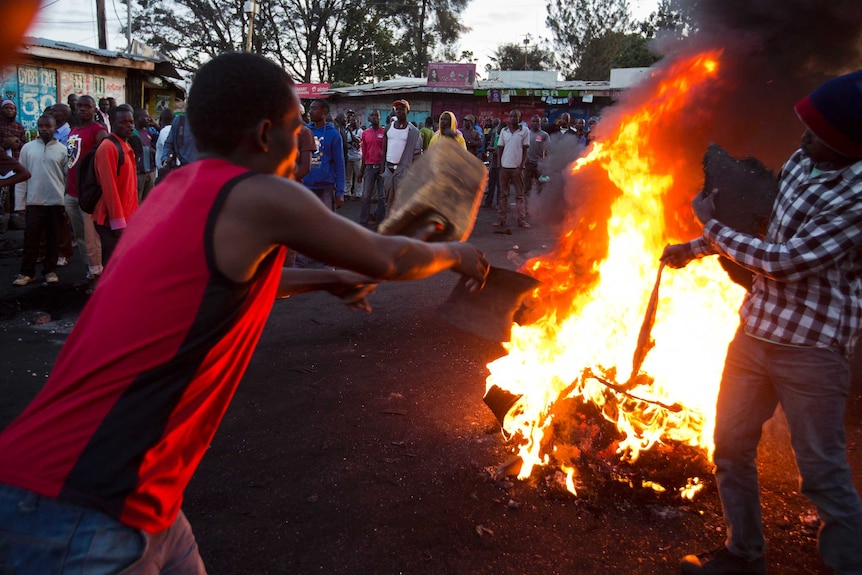 People throw objects into a fire burning on a street.