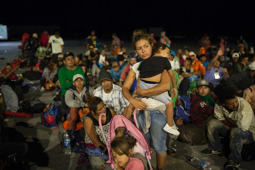 A woman holds a young child amid a number of other Central American migrants.