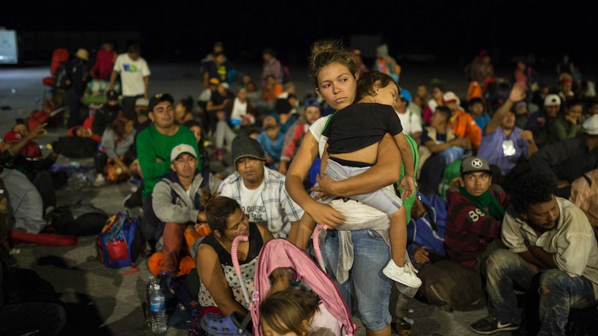 A woman holds a young child amid a number of other Central American migrants.