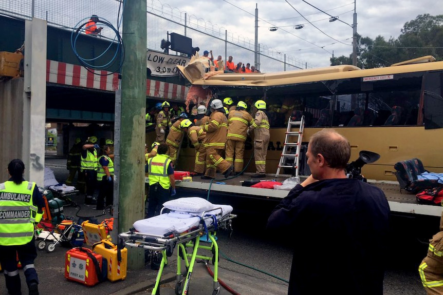 Emergency crews work to free passengers from the bus which is wedged under the bridge.