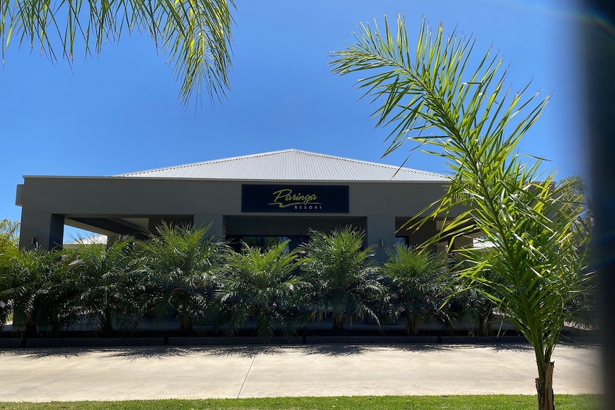 A modern grey cement building with palm trees out the front and a sign that says 'paringa resort'