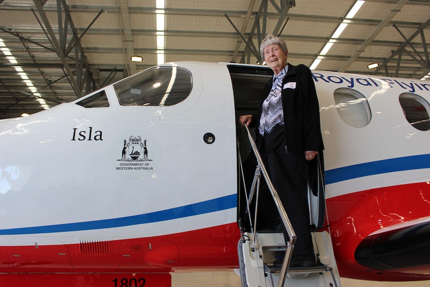 An older woman standing in the door of an aircraft that was Royal Flying Doctors Service written across it