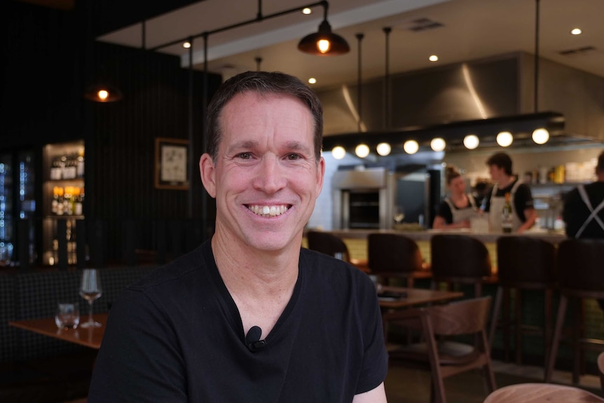 A man in his twenties smiles in a restaurant