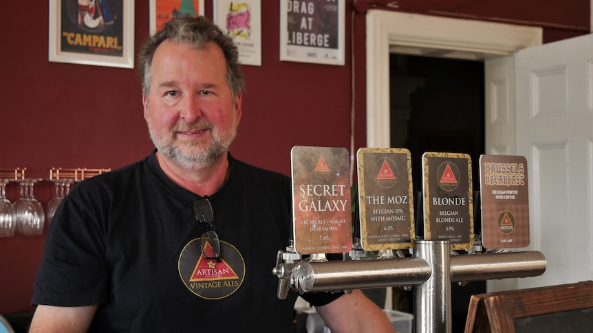 A bearded man with short grey hair stands behind a bar.