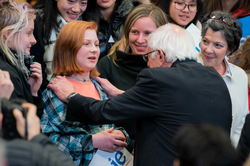 Bernie Sanders holds a supporters' shoulders while others look on at a campaign event.